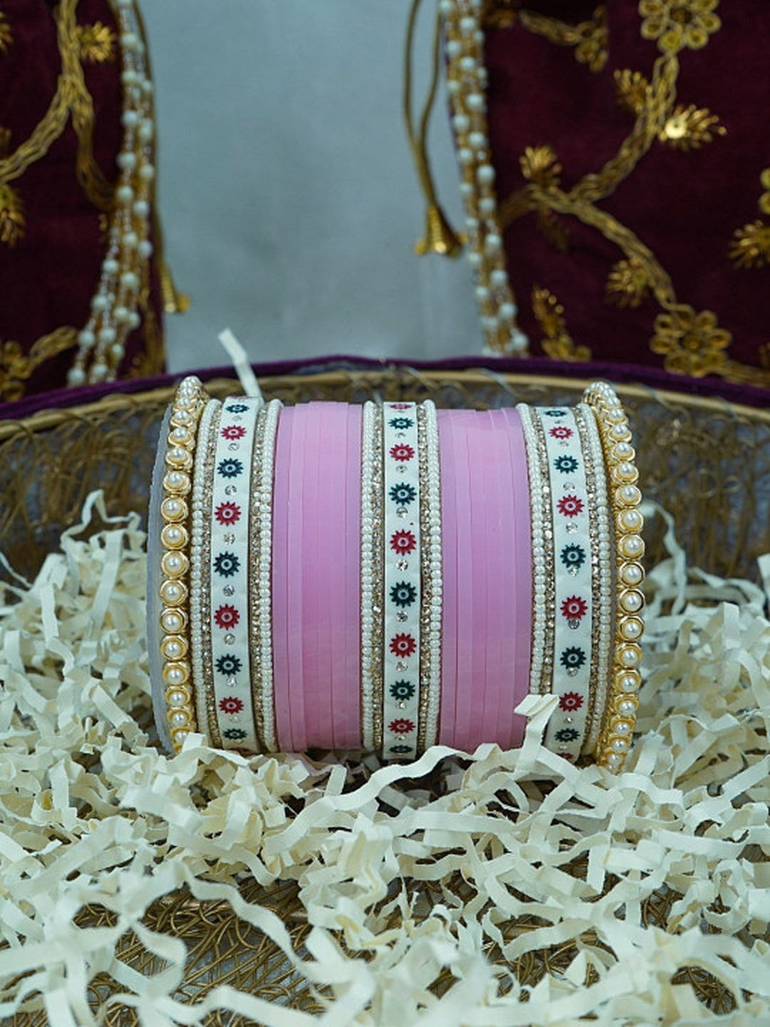 Ishhaara Pink Bangle Set - a beautifully crafted set of pink bangles with pearl embellishments arranged in a decorative bowl with shredded paper