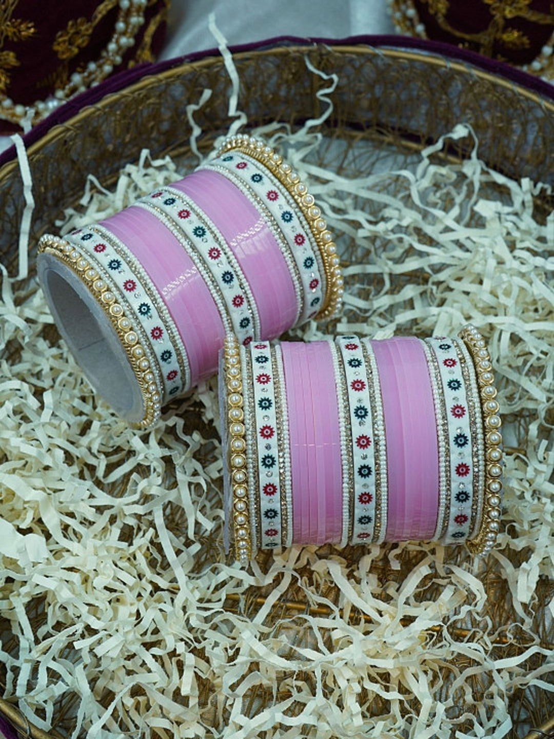 Ishhaara Pink Bangle Set - a beautifully crafted set of pink bangles with pearl embellishments arranged in a decorative bowl with shredded paper - view 2