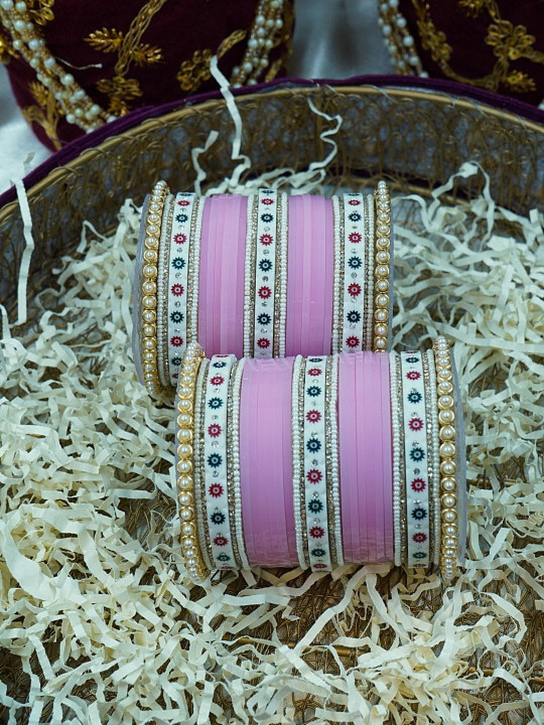 Ishhaara Pink Bangle Set - a beautifully crafted set of pink bangles with pearl embellishments arranged in a decorative bowl with shredded paper - view 4